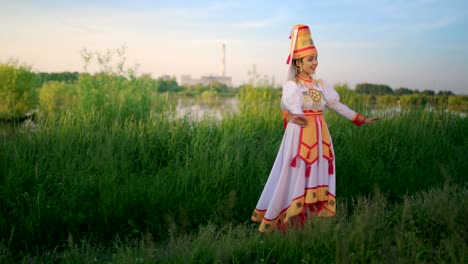 привлекательная молодая женщина в традиционном костюме марийцев танцует на луге