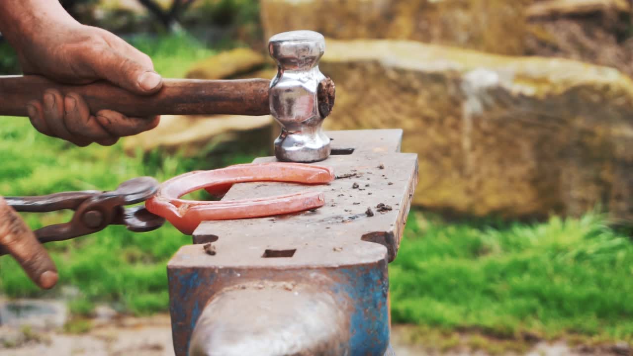 un herrador que da forma a un zapato rojo brillante para que se ajuste a los cascos de un caballo joven