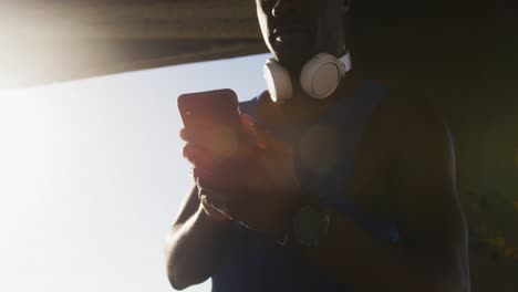 african american man checking smartphone taking break during exercise outdoors by the sea