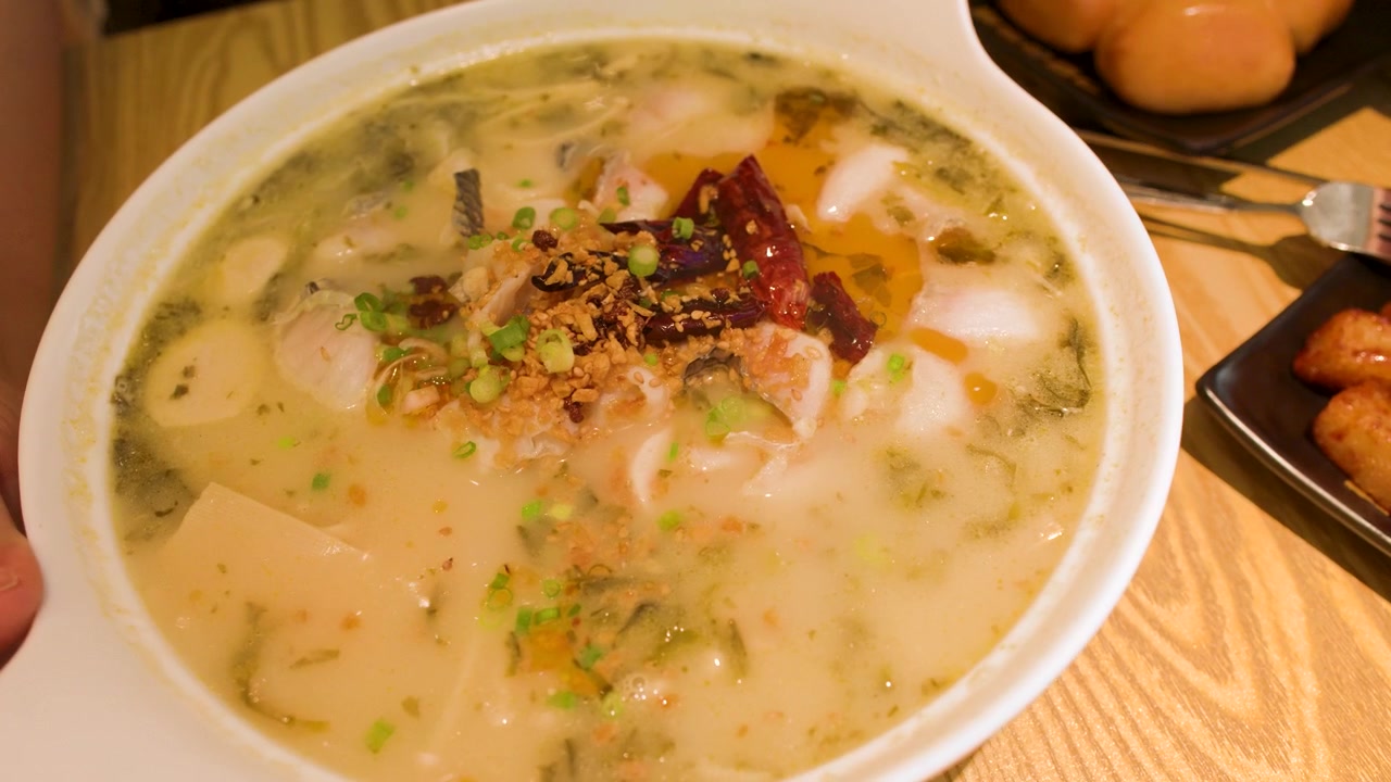 Nærbillede af dampende krydret fiskesuppe med syltede grøntsager og chili på restaurant