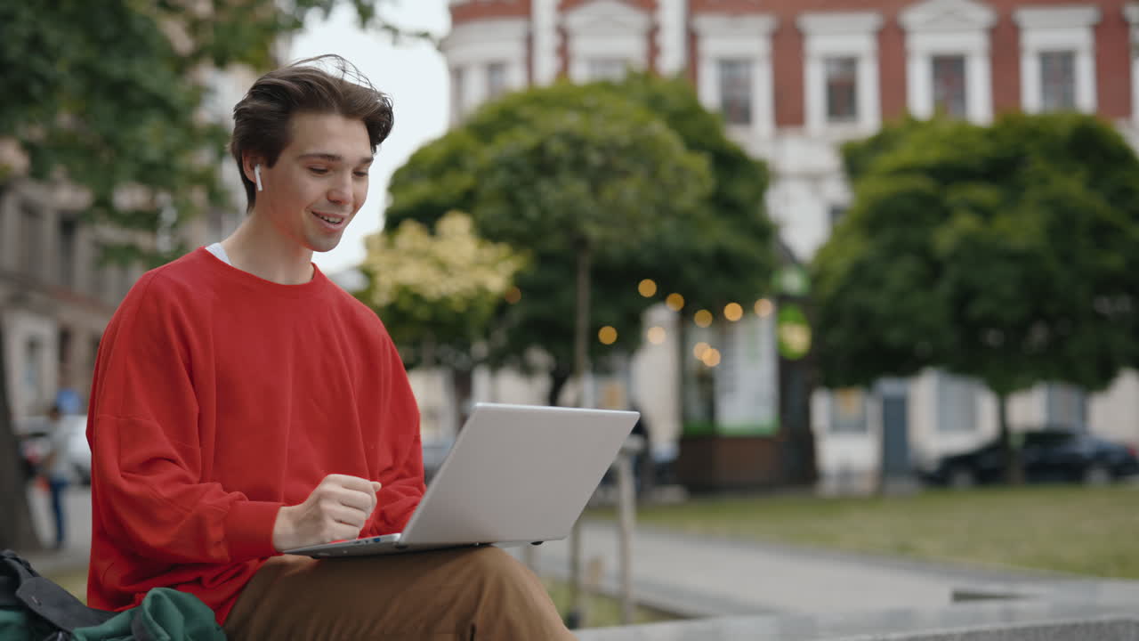 Giovane uomo che lavora al computer portatile in un parco urbano
