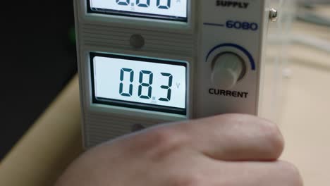 vista de primer plano de la mano de una persona ajustando un suministro de voltaje en una pantalla digital, mostrando un control preciso en un entorno de laboratorio