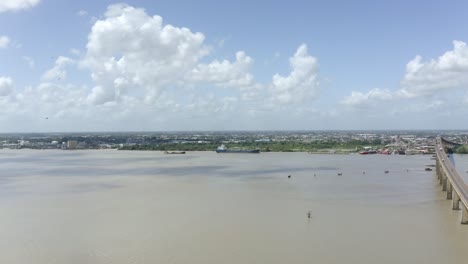 Wide-angle-drone-view-orbiting-oil-tanker-ship,-Jules-Wijdenbosch-bridge-nearby-flyover