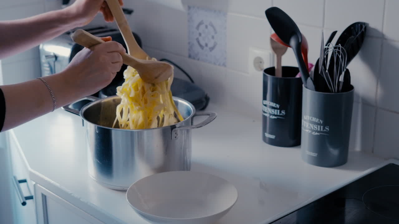 Woman putting Pasta Tagliatelle from steaming Pot into the plate with two wooden Spoons in slow motion during a day