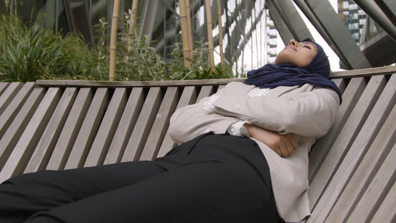 Muslim Businesswoman Resting On Bench Outdoors In City Gardens Or Park