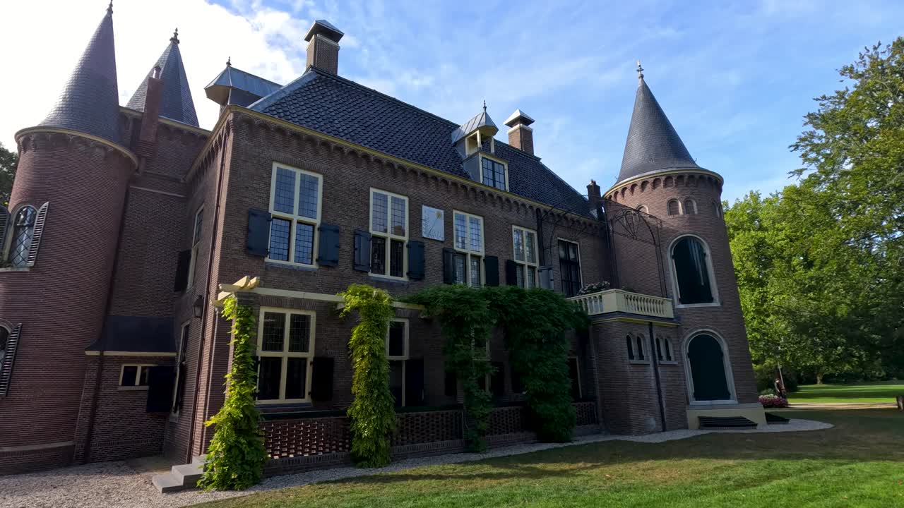 A smooth daytime camera pan reveals a brick castle with turrets and lush botanical gardens under clear blue skies in Lisse, Netherlands