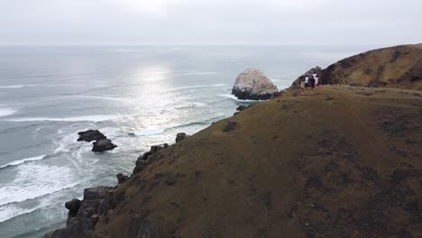 aerial 360 of hikers standing atop steep cliffside with amazing mountain and ocean views all around them