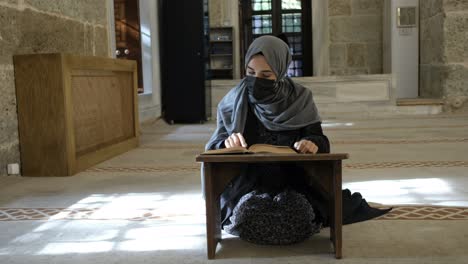 masked muslim woman reading quran in mosque