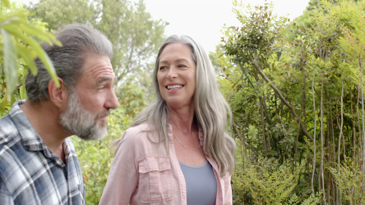 Smiling mature couple enjoying nature, pointing at trees in lush garden