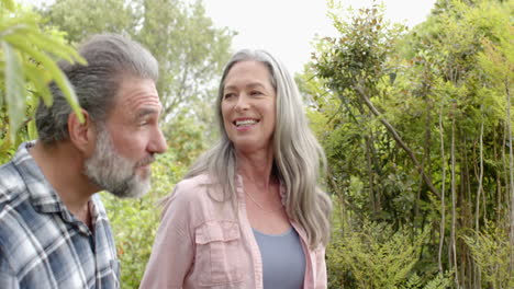 smiling mature couple enjoying nature, pointing at trees in lush garden