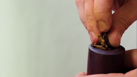 caucasian male hand filling up vintage pipe with fresh tobacco inside the hole on cloudy day on his balcony time to relax and enjoy quiet time while smoking like in the old days white background