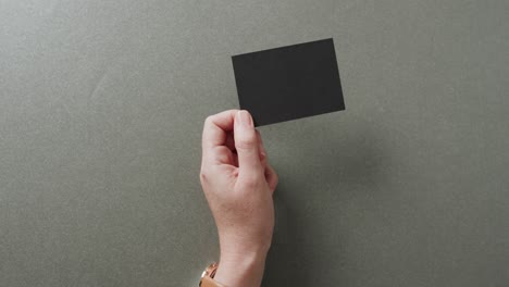 Hand-of-caucasian-woman-holding-black-business-card-on-grey-background,-copy-space,-slow-motion