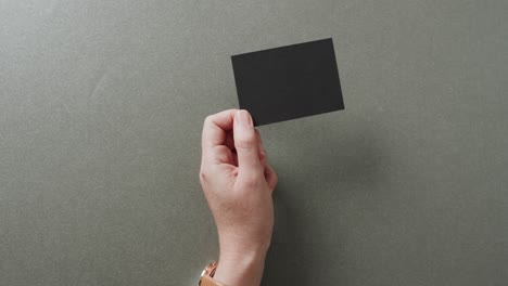 hand of caucasian woman holding black business card on grey background, copy space, slow motion