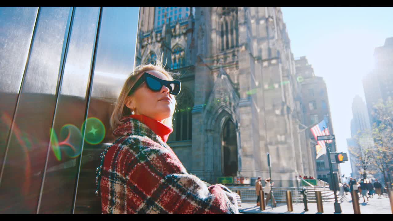 New York, USA, 9 ottobre 2025: Profilo di donna che guarda in alto vicino alla Cattedrale di San Patrizio a Manhattan. Donna con cappotto a quadri appoggiata a un muro che guarda la cattedrale gotica a New York City con bagliore dell'obiettivo.