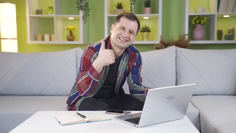 hombre haciendo un gesto positivo con la mano mientras sonríe a la cámara mientras trabaja en la computadora portátil.