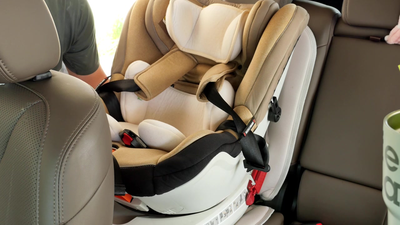 Un hombre ajusta una silla de coche para niños dentro de un vehículo. El entorno está bien iluminado, destacando el diseño y las características de seguridad de la silla. Útil para tutoriales de paternidad y guías de seguridad.