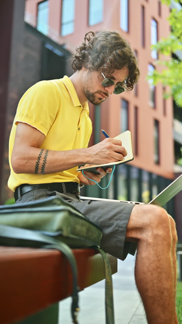 Man in yellow shirt talking standing on a bench and writing in a notebook. Vertical