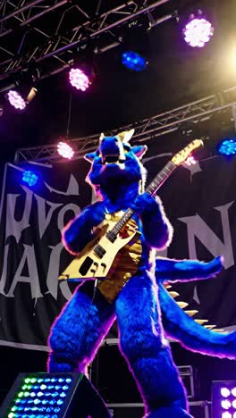 blue dragon mascot wearing a gold vest plays an electric guitar on stage, captivating the audience during a live concert filled with vibrant, colorful lights and energetic performance