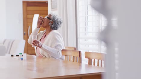 Senior-african-american-woman-sitting-at-table,-taking-pills