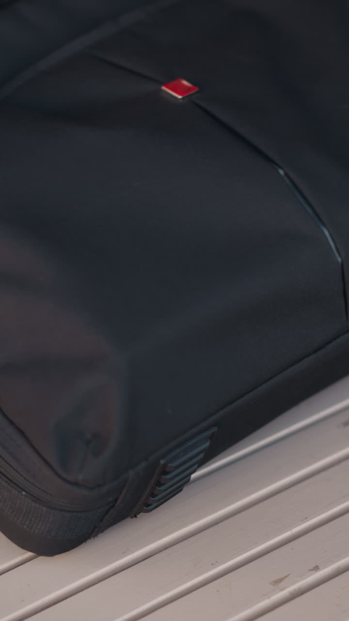 Close-up of someone in black coat dropping a bag on a wooden table and unzipping it, showcasing white polished nails in a blurred urban outdoor setting
