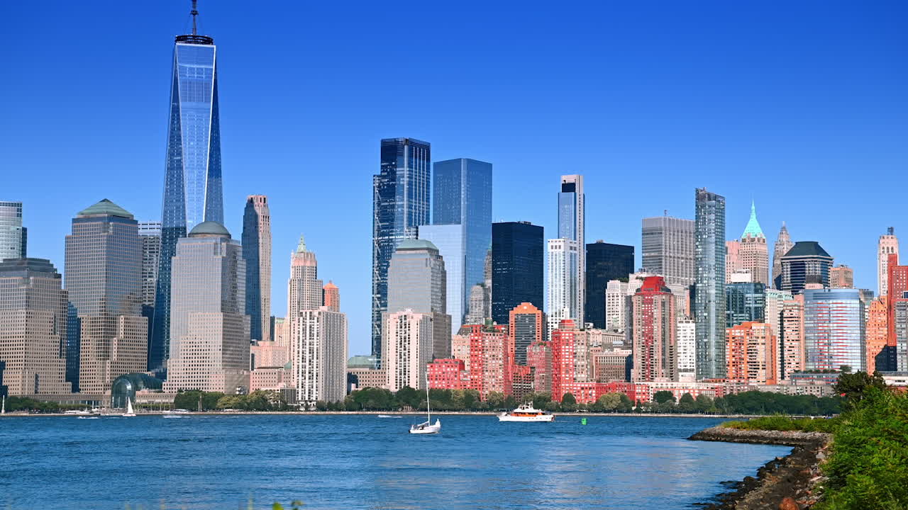 Several boats move by the waterscape of the Hudson River. Manhattan skyline from Jersey on sunny day