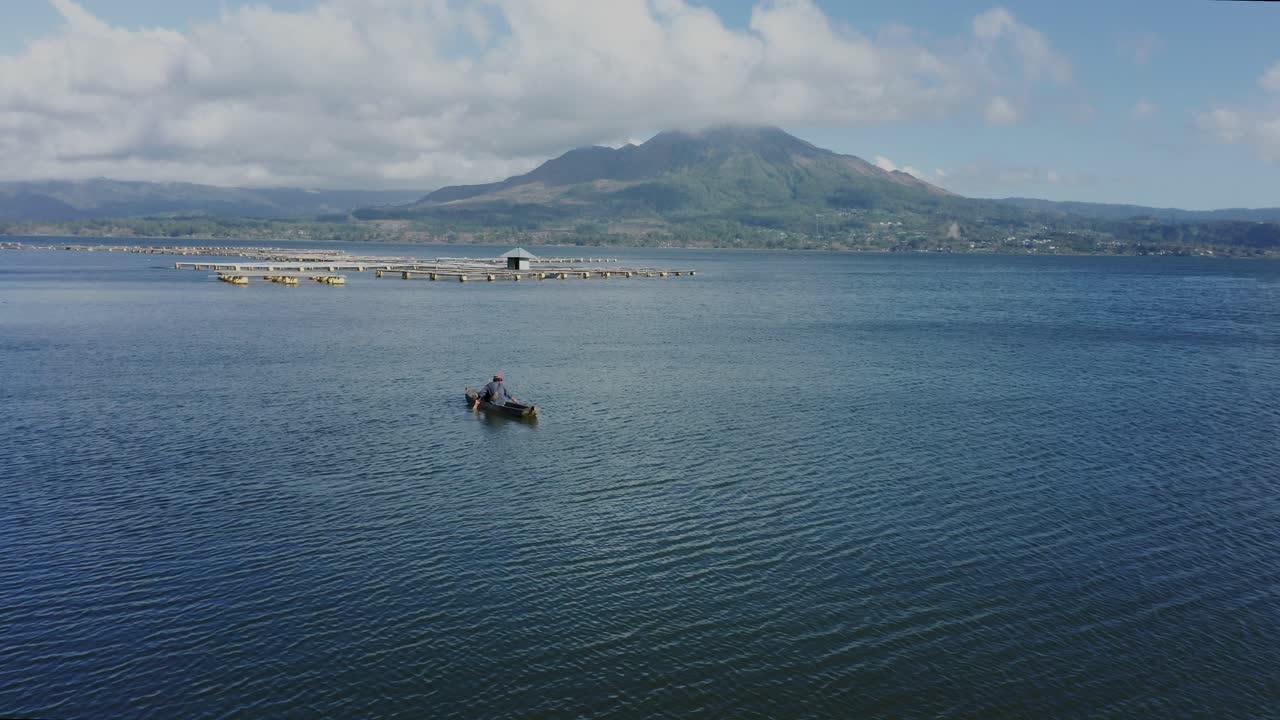 Local fisherman checking his nets for fish with fish farms floating in background, lake Batur, aerial