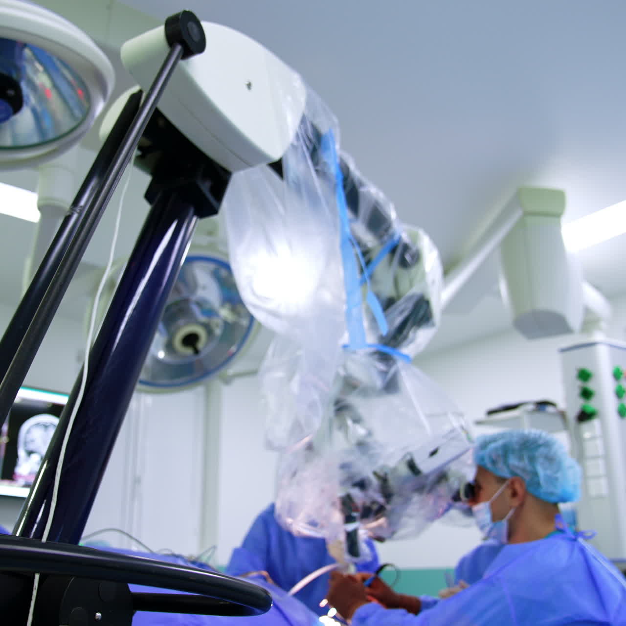 Male Caucasian neurosurgeon sits in front of microscope. Low angle view on the medical equipment in operational theatre.