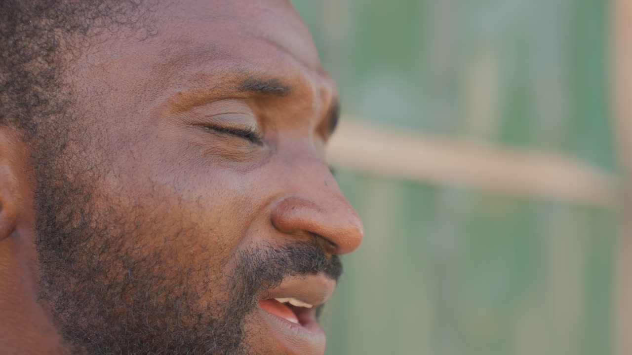Athlete practicing deep breathing outdoors, closeup profile with green fence background, soft gaze, relaxed jaw, sunlit skin, mindfulness after training, steady inhalation, cooling down, serene mood