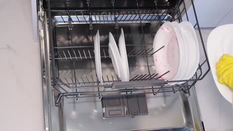 video female hand in rubber gloves puts white plates in the dishwasher