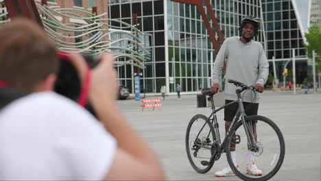 Photographer-takes-a-picture-of-a-young-man-posing-beside-his-bicycle-downtown