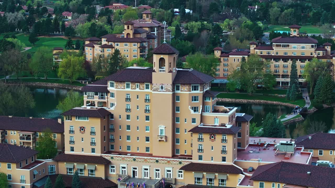 Curved paths and lake accent Broadmoor resort surrounded by forest and light, aerial telephoto summer orbit