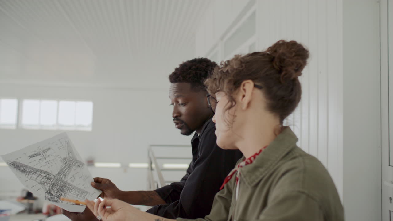 Two Diverse Colleagues Discussing Aircraft Blueprint in Aviation Hangar