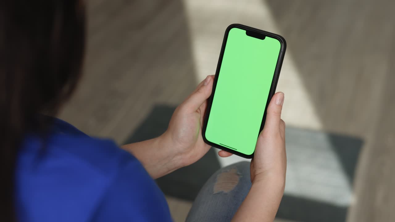 vista trasera de una chica morena sosteniendo una llave de croma pantalla verde simulacro de teléfono inteligente viendo contenido sin tocar o deslizar. usar pantalla verde para copiar espacio. aparatos y conceptos de personas contemporáneas