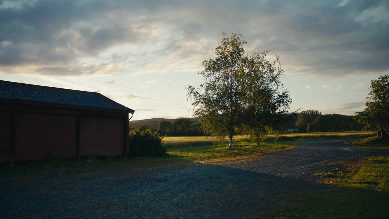Traditionel norsk bondegård med rustik lade, åbne marker og varmt aftenlys, der fanger den fredfyldte skønhed af en landlig sommer.
