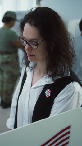 retrato de una mujer soldado, votante de las elecciones de los estados unidos de américa. una mujer en uniforme de camuflaje se para en la estación de votación y mira a la cámara. fondo con cabinas de votación. concepto de deber cívico.