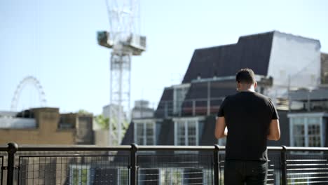 european athletic build male wearing glasses, checking his smartphone on a sunny rooftop with cityscape background pacing up and down