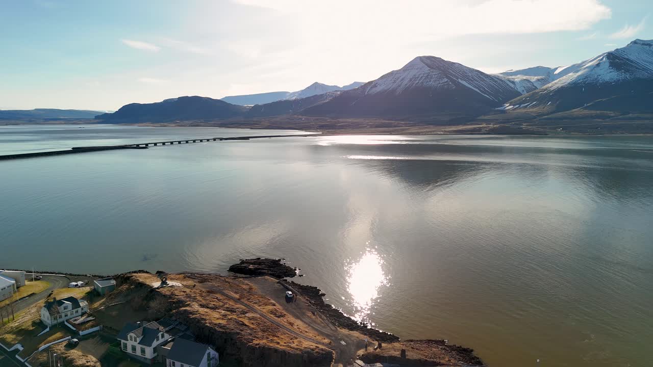 Flying out from Borgarnes over the fjord water towards a bridge crossing the water towards a spectacular mountain landscape Hafjarfjall in the distance