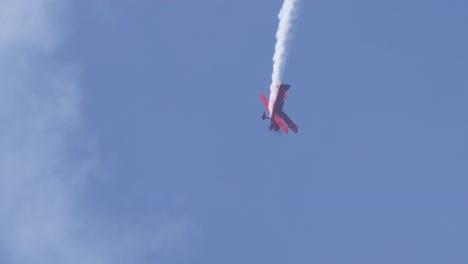 red plane executes aerial maneuvers with smoke trail