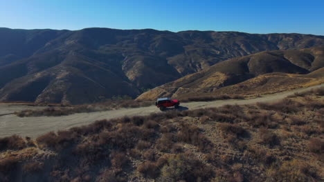 Epic-aerial-view-of-offroad-red-Jeep-climbing-trail-on-top-of-desert-hills