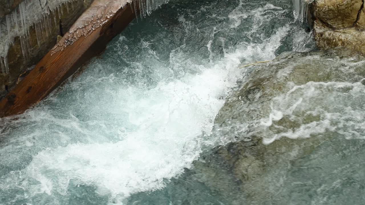 Cold clear water of river stream splashing on frozen cliffs with ice stalactites on a winter day