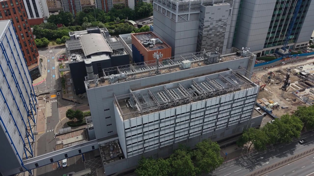 Una prospettiva aerea cattura un grande edificio moderno di data center situato in un ambiente urbano durante il giorno. Adiacente ad esso, un cantiere con macchinari pesanti è attivo.