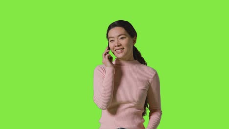 fotografía de estudio de una mujer sonriente respondiendo al teléfono móvil contra una pantalla verde