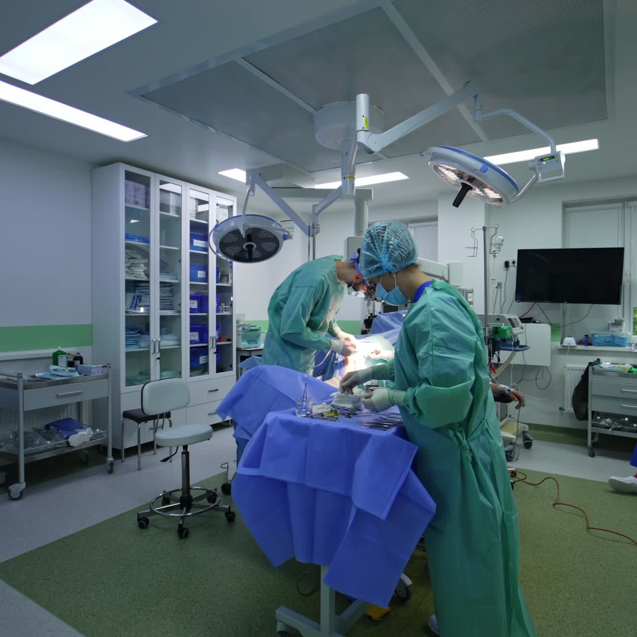 Entering the modern well-equipped surgery room. Nurse arranges instruments on the table and doctors performing surgical operation