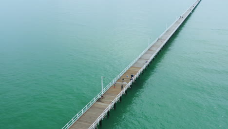 Aerial-4K-Drone-Flyover-Long-Pier-Boardwalk-With-Athlete-Running-Along-Pathway