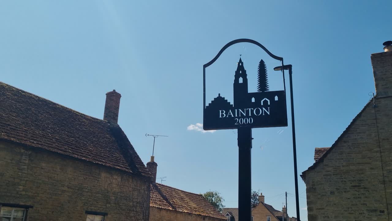 Bainton village sign with historic Butter Cross, unveiled in 2000 via the Buttercross Millennium Fund, Cambridgeshire landmark linking past and present under a blue summer sky