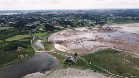 Backward-Drone-Shot-over-Brittany's-Shore-at-Low-Tide-Showing-Rocky-Landscape-and-Houses,-France