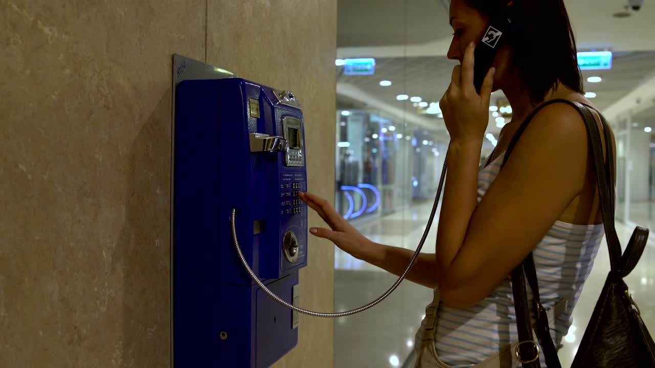 The woman approaches the telephone and answers the phone and dials the number