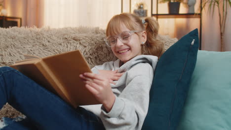 young small teenager girl reading favorite storybook at home sofa quiet smiles tiny serious sighs