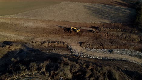 Yellow-excavator-standing-on-the-construction-of-a-new-road-in-the-middle-of-the-fields-at-sunset