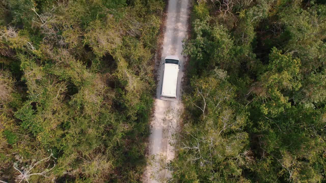 Mini van driving on a sand road through the forest of Tulum, Mexico top down aerial view